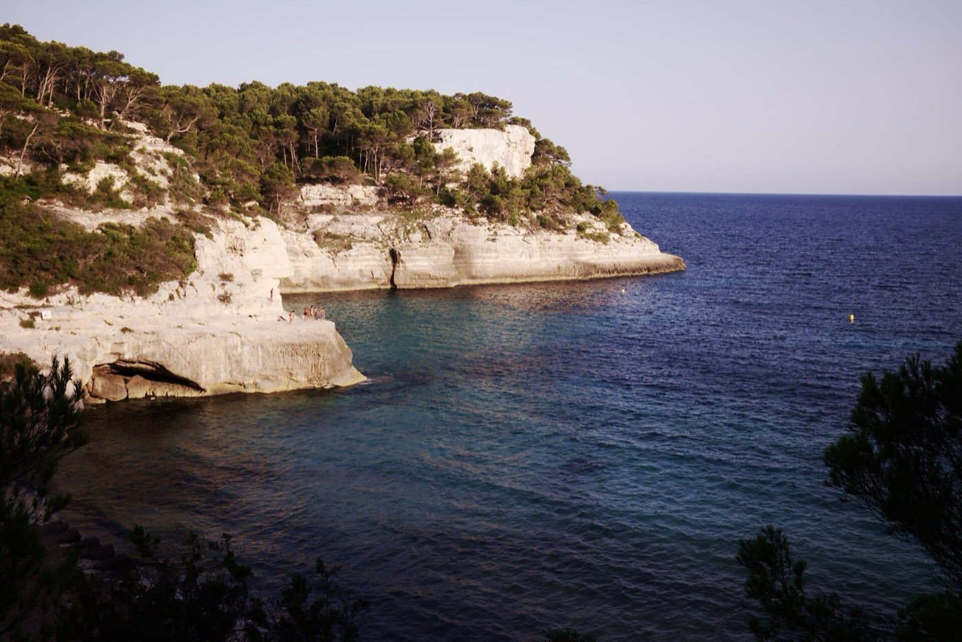Cala de aguas azules entre acantilados blancos y pinos en Menorca